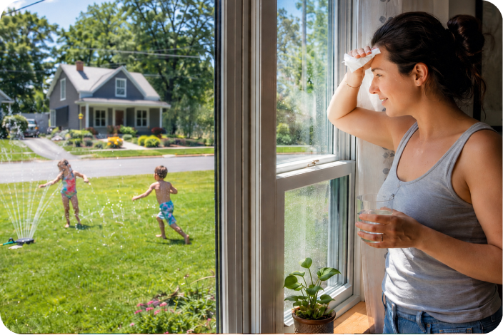 Image of a woman watching her children play in a sprinkler